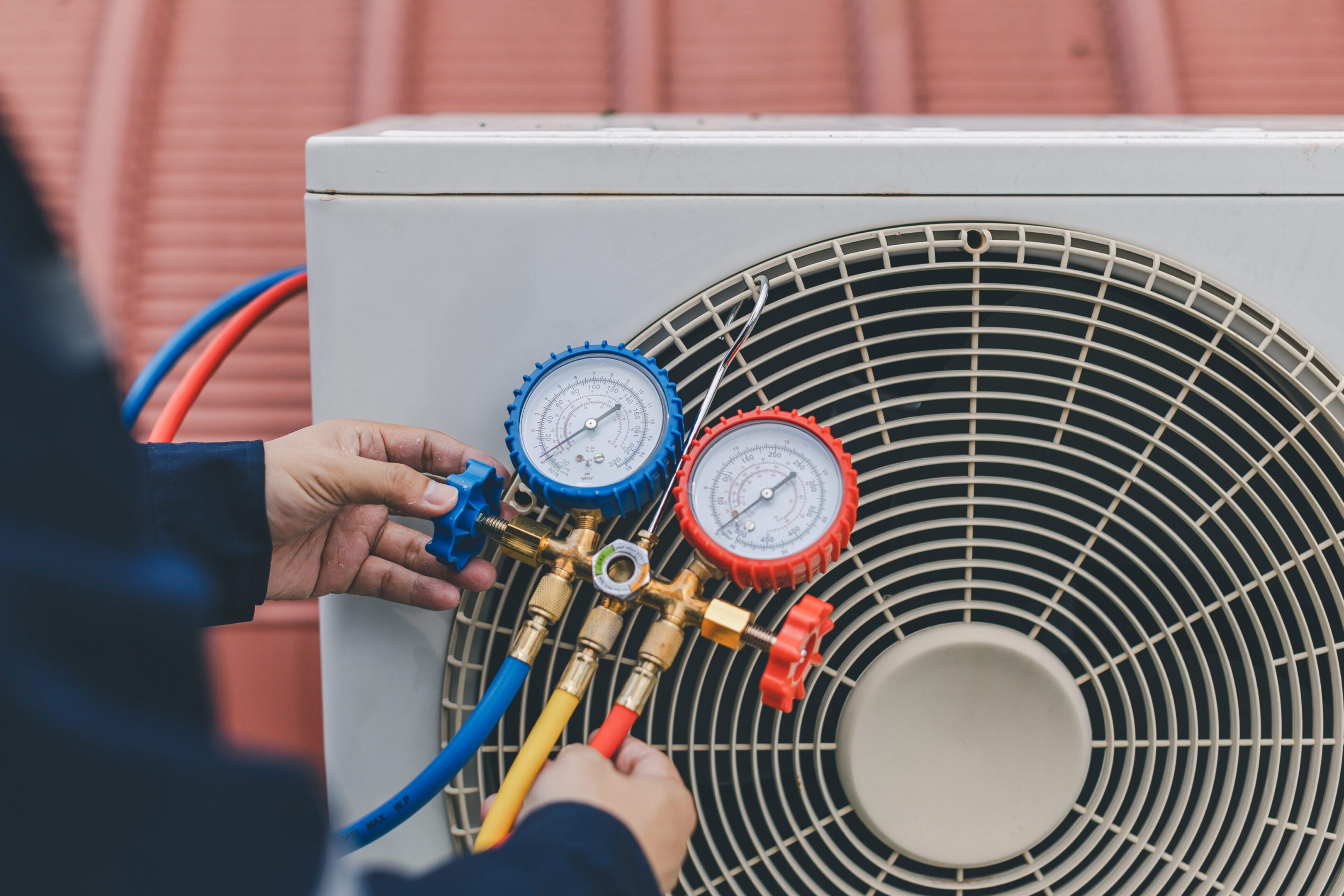 Technician is checking air conditioner. Air conditioning, HVAC service technician using gauges to check refrigerant and add refrigerant. Person adjusting gauges on an air conditioning unit with red and blue hoses.